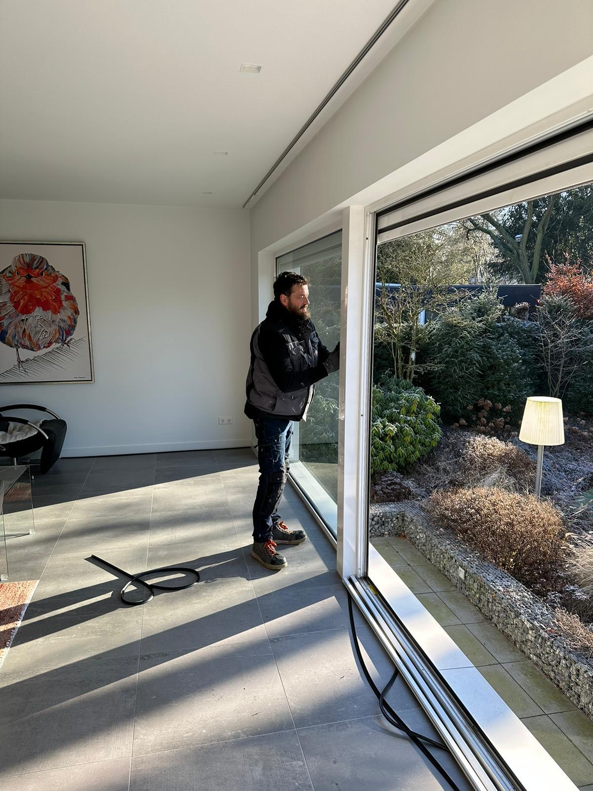 Een man staat voor een groot raam in een woonkamer.