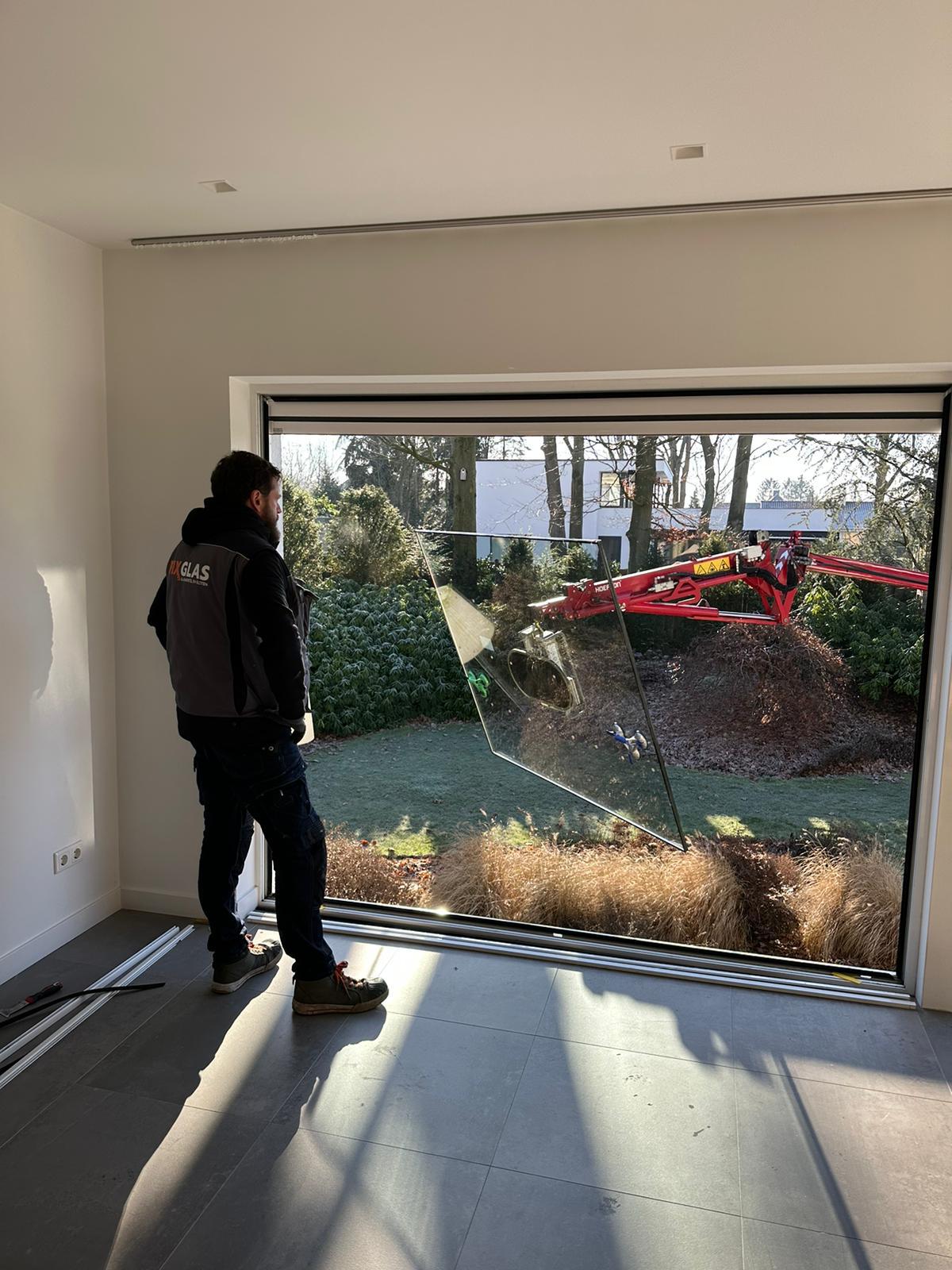 Een man staat voor een groot raam en kijkt naar buiten.