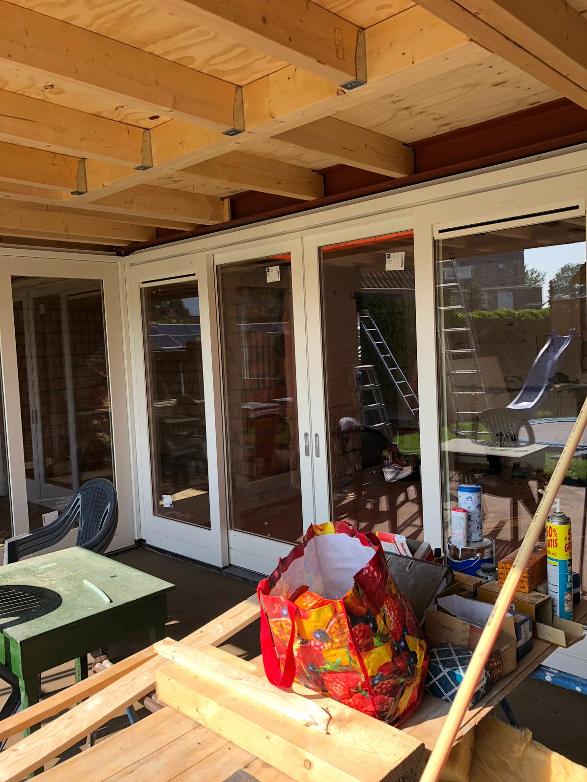 Een rode tas ligt op een houten tafel in een kamer met veel ramen.