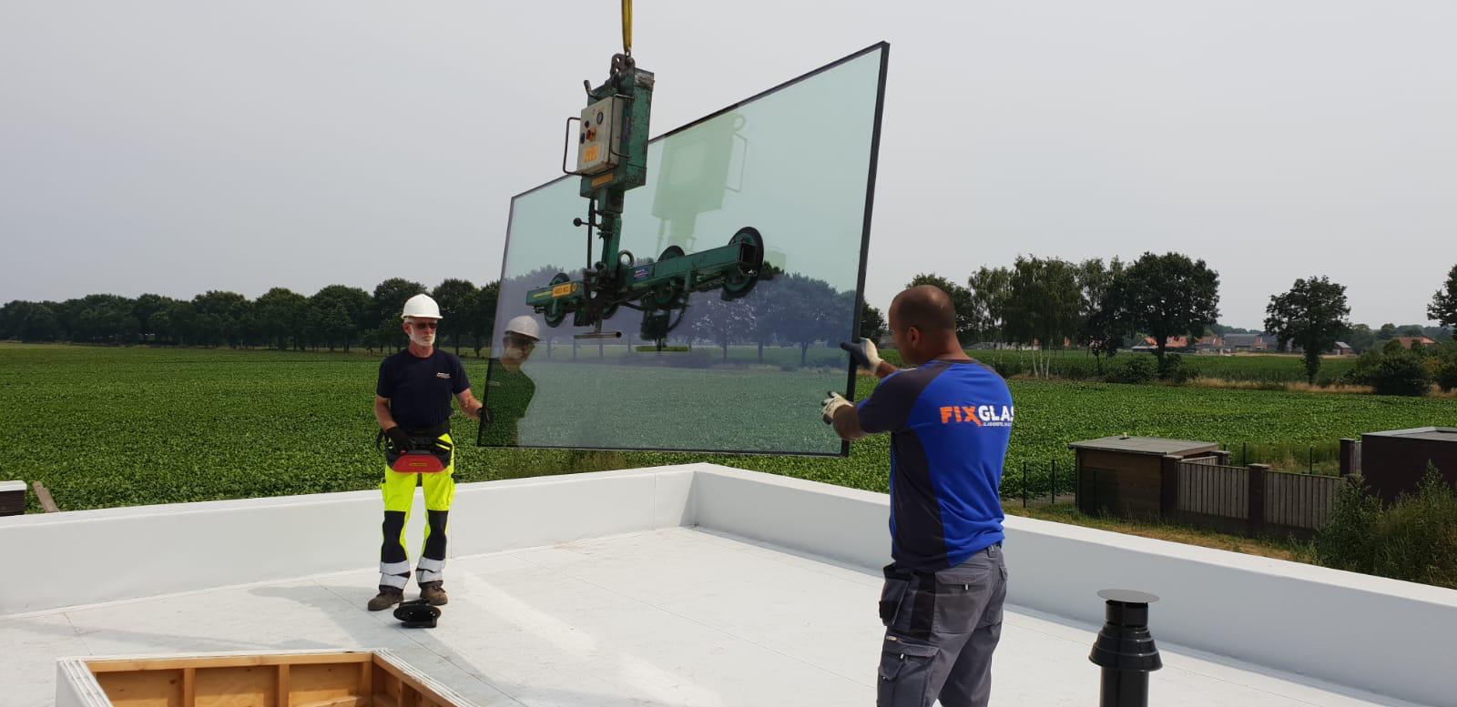 Twee mannen staan ​​op een dak en houden een groot stuk glas vast.
