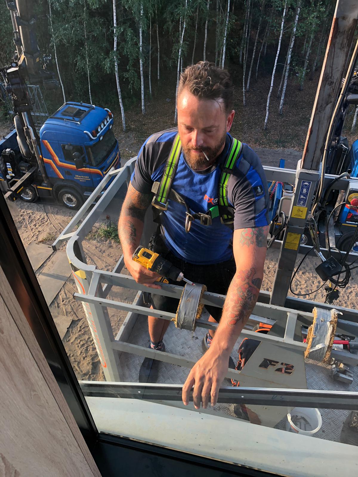 Een man zit in een kooi met een boor in zijn handen.