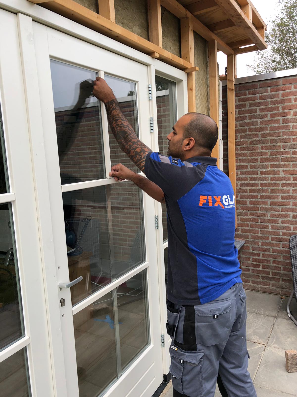 Een man in een blauw shirt installeert een raam in een deur.
