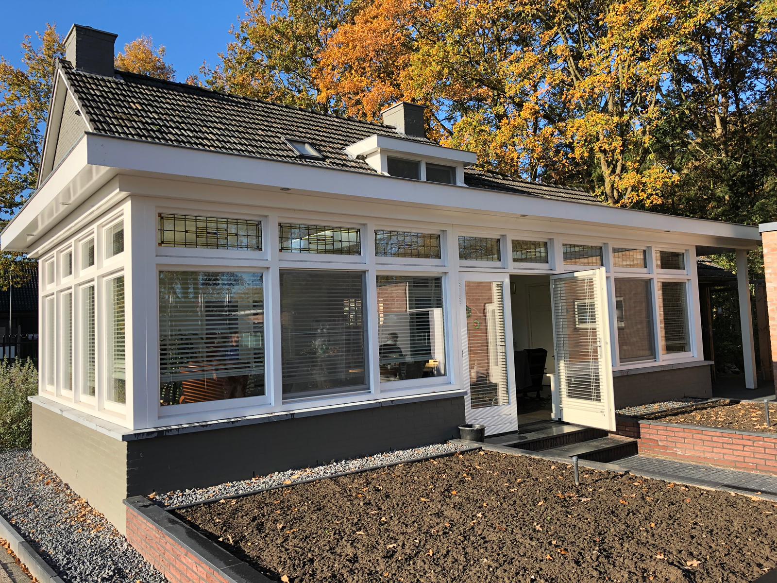 Een klein huis met veel ramen en deuren, omgeven door bomen.