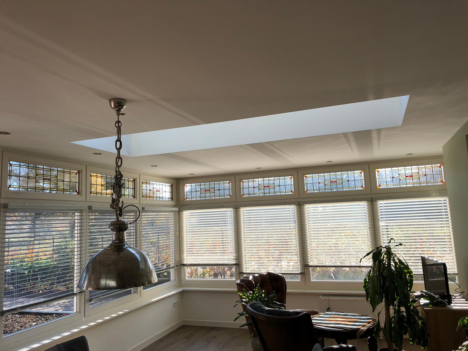 Een woonkamer met veel ramen en een dakraam.