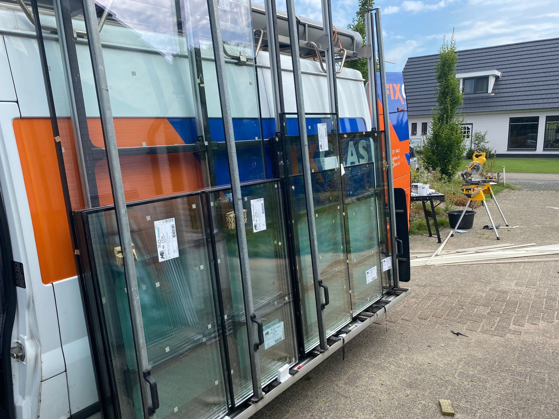 Een busje met veel glas erop staat voor een huis geparkeerd.