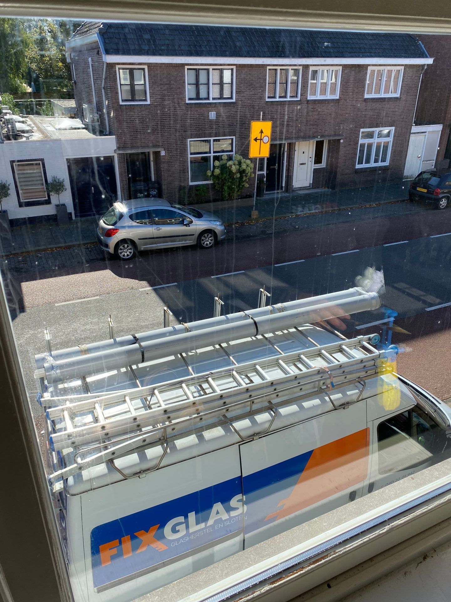 Een busje met daarop een ladder staat geparkeerd voor een gebouw.