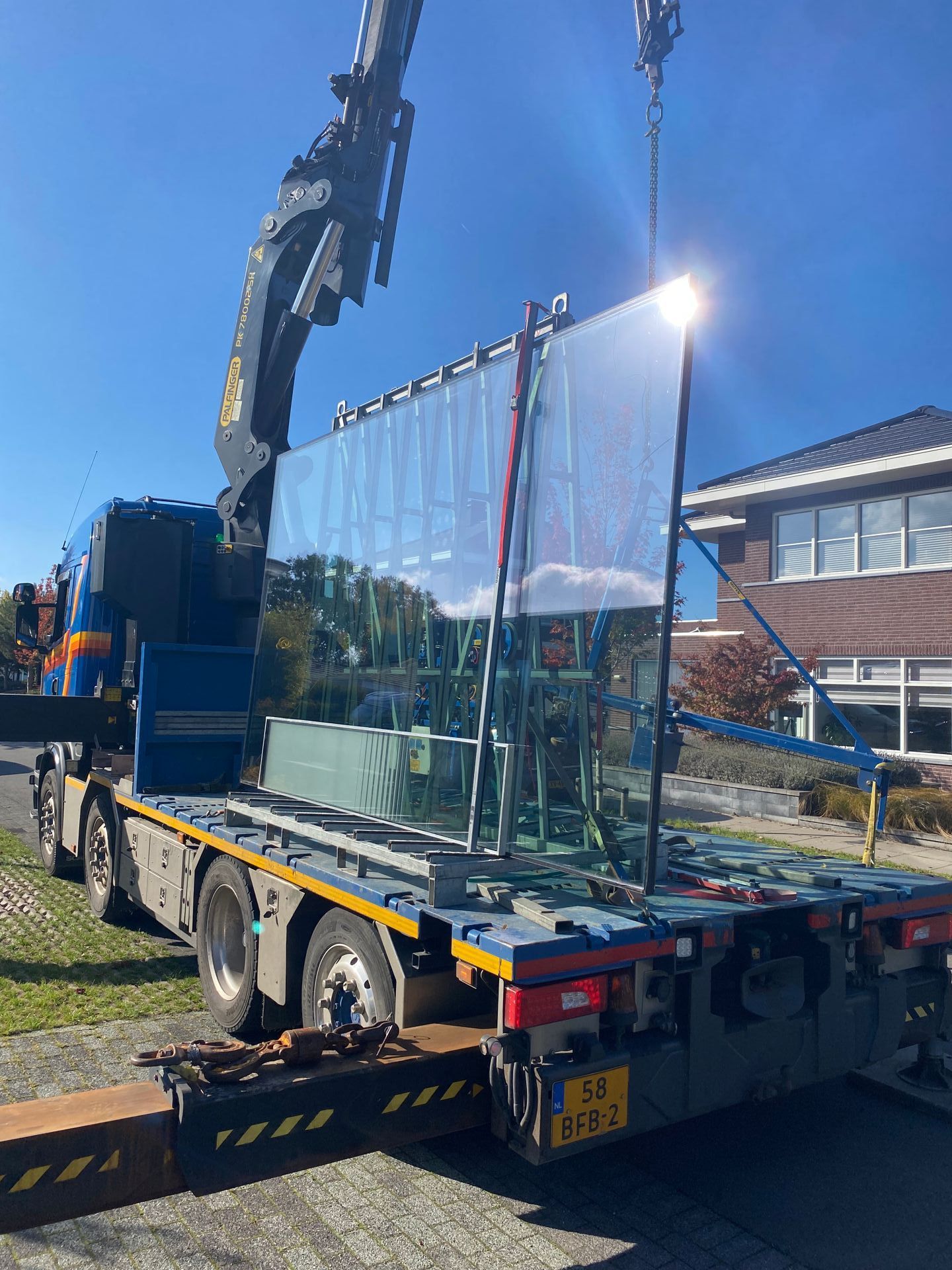 Een groot stuk glas wordt door een kraan op een vrachtwagen gehesen.