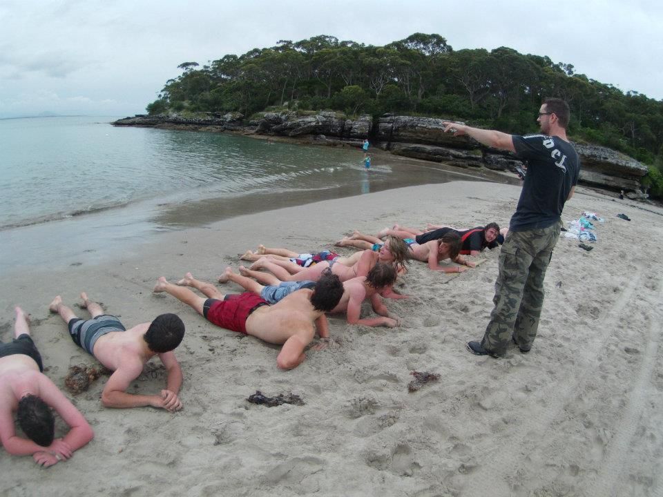 A group of people are doing push ups on the beach