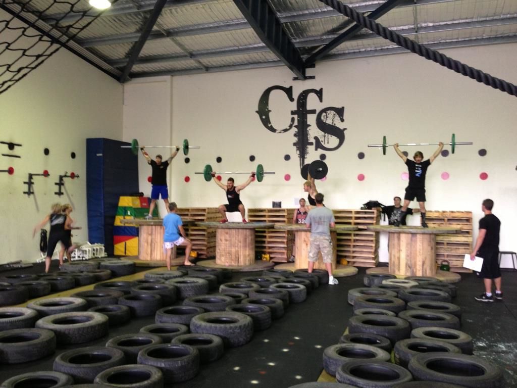 A group of people are working out in a gym with the word cfs on the wall