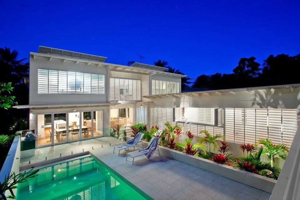 Modern Two-story House With a Pool, Patio, and Lush Landscaping at Dusk — Keilbach Kitchens in Mission Beach, QLD