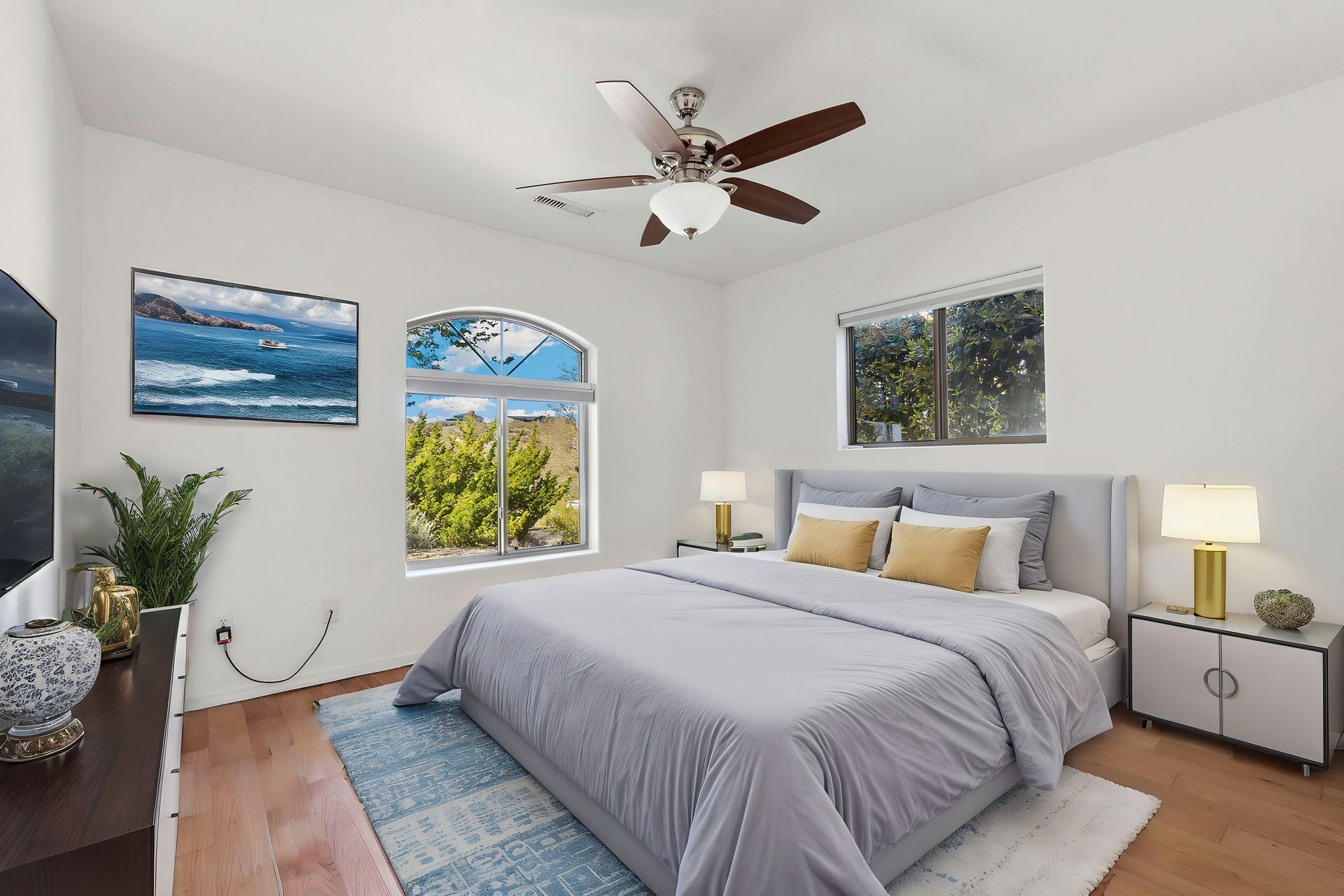Bedroom with bed, nightstands, and windows; white walls, wooden floor, blue and gold accents.