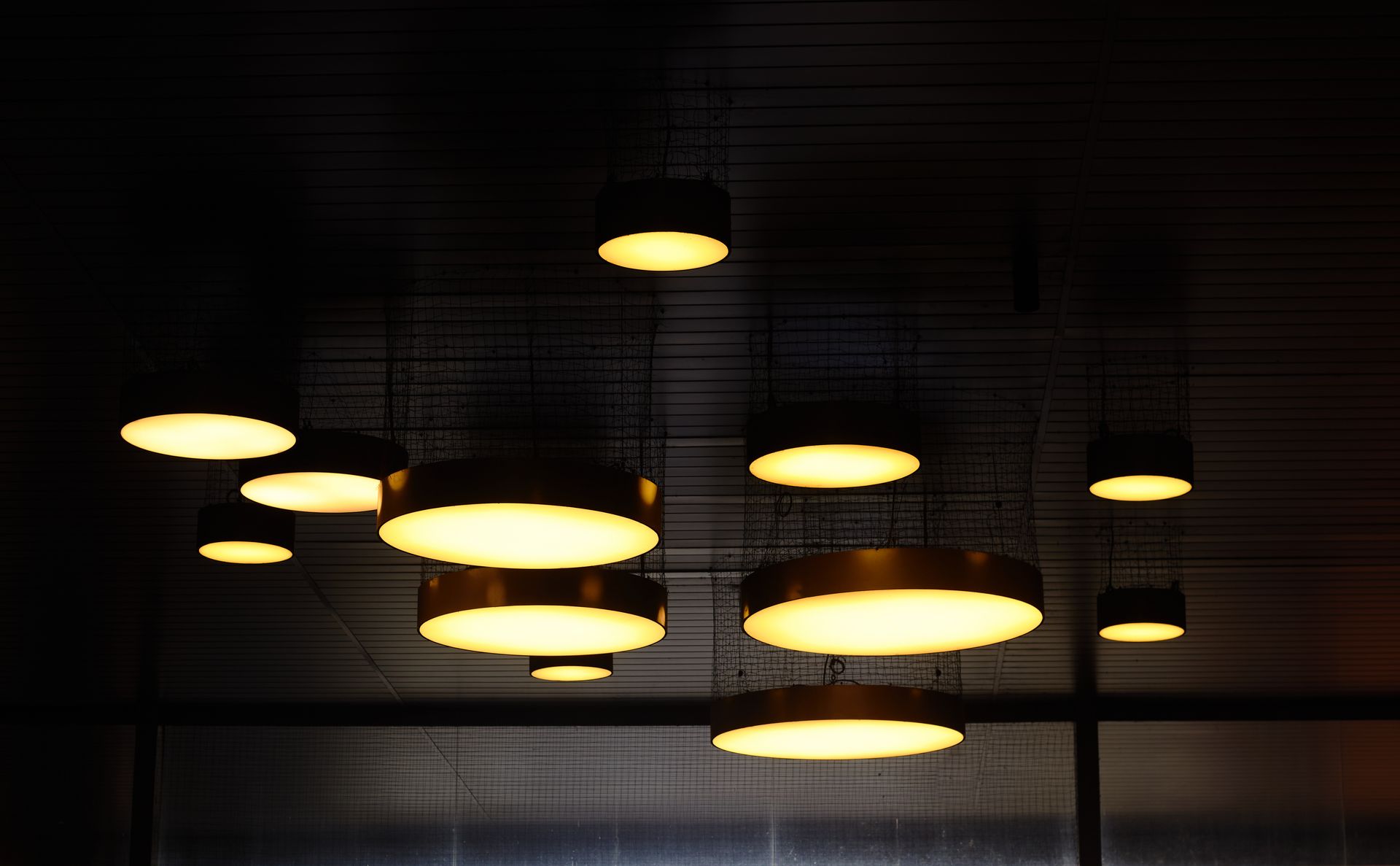 Hanging ceiling lights, each a golden, glowing disc, against a dark background.