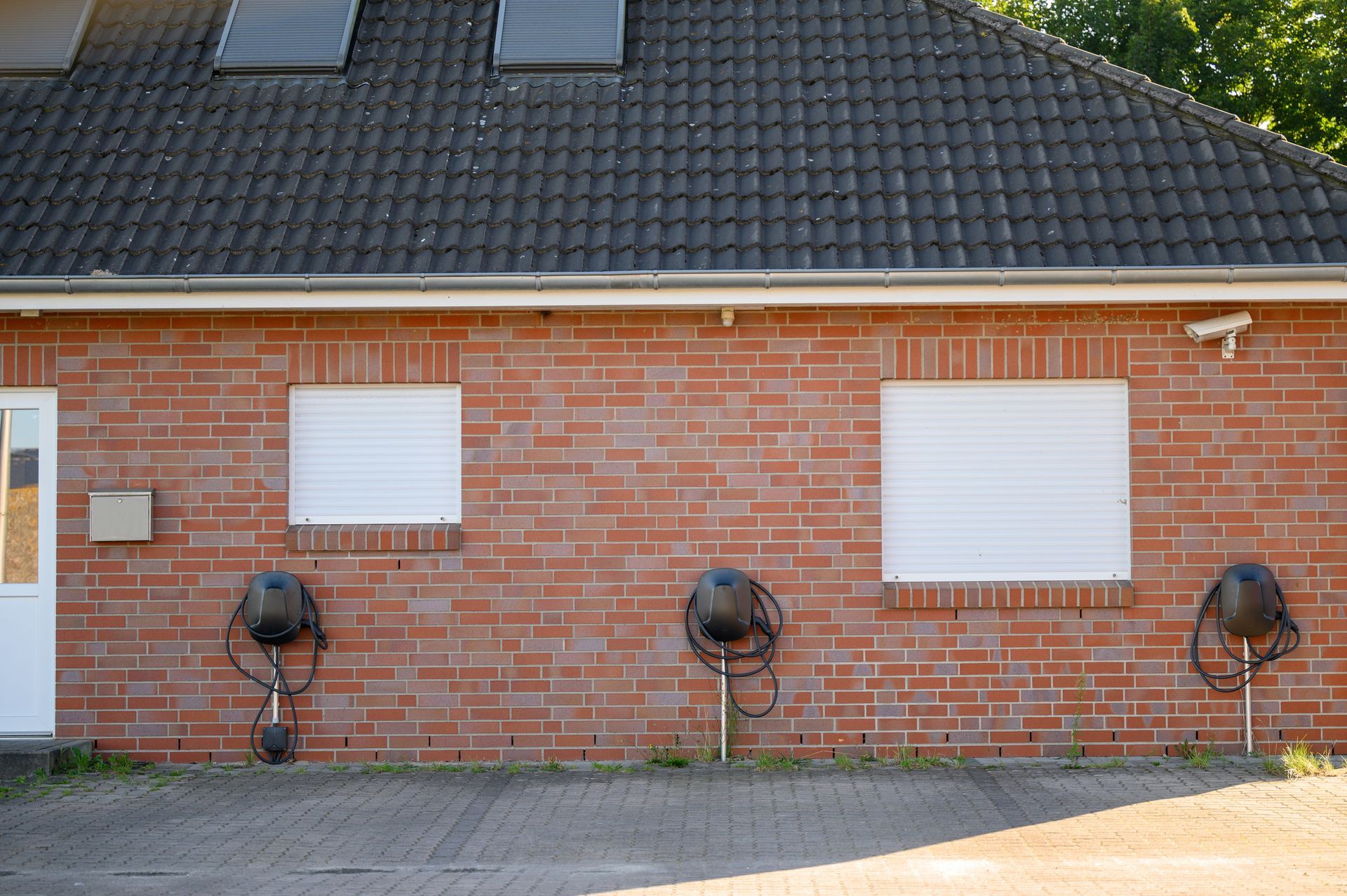 Red brick building with two white-covered windows, three black hose reels, and a gray roof.