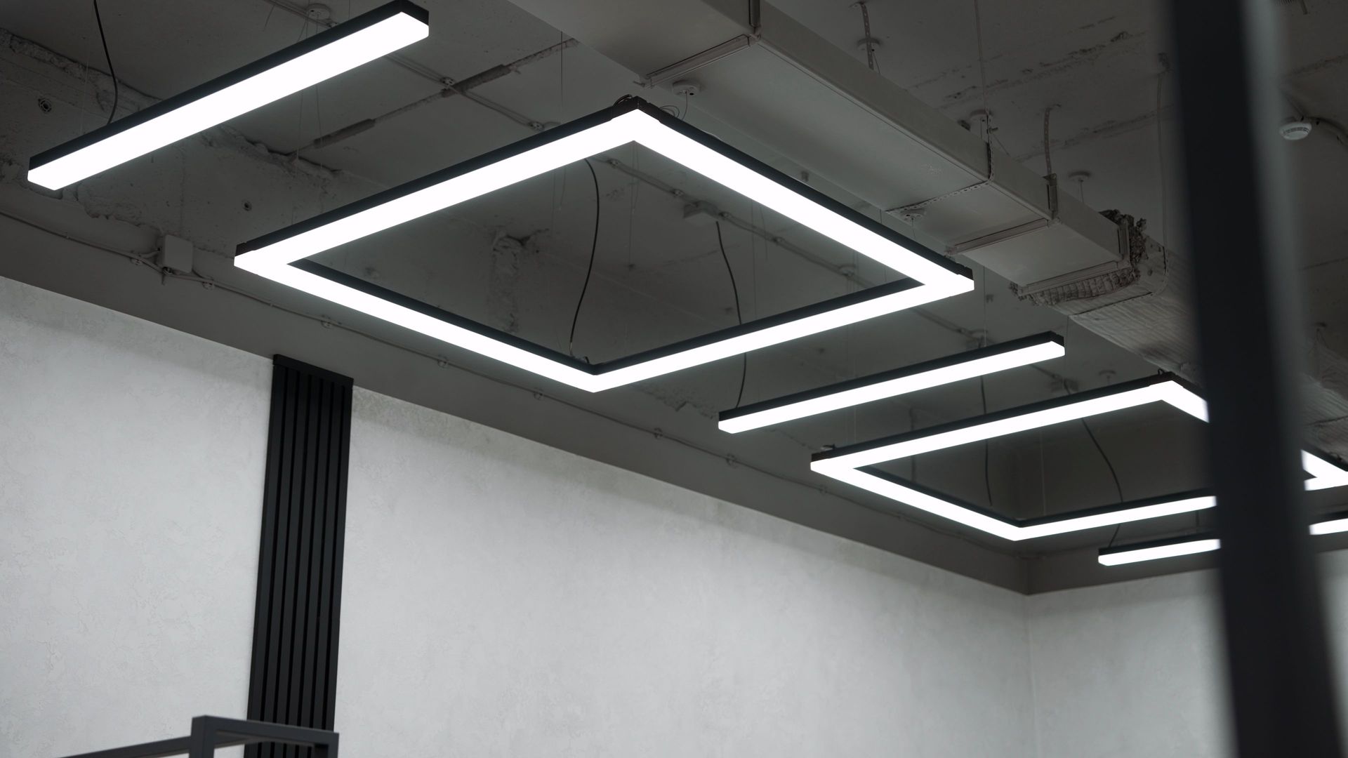 Bright square and rectangular lights hanging from a gray ceiling in a room.