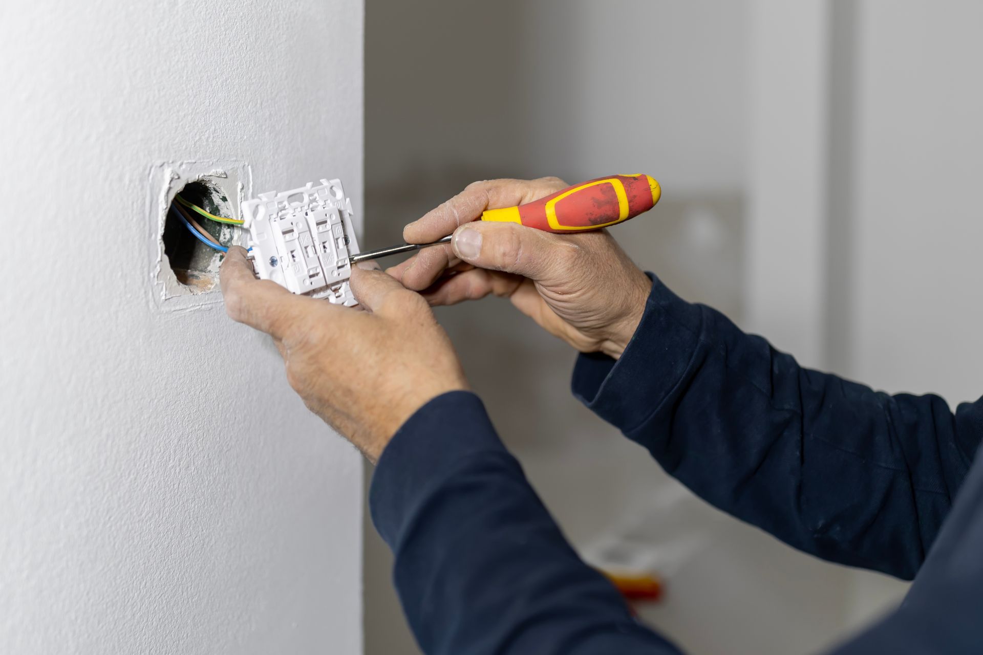 Person installing electrical outlet with screwdriver in a wall.