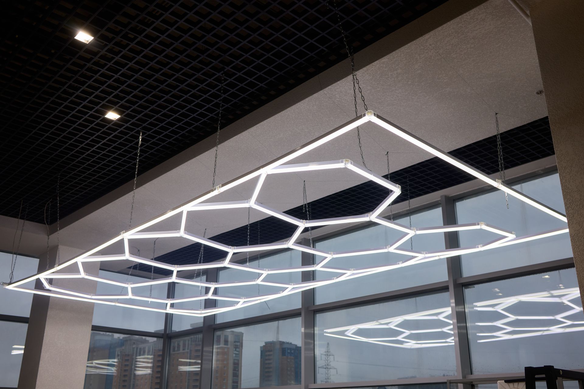 Geometric ceiling light fixture, honeycomb pattern, hanging in a room with large windows.