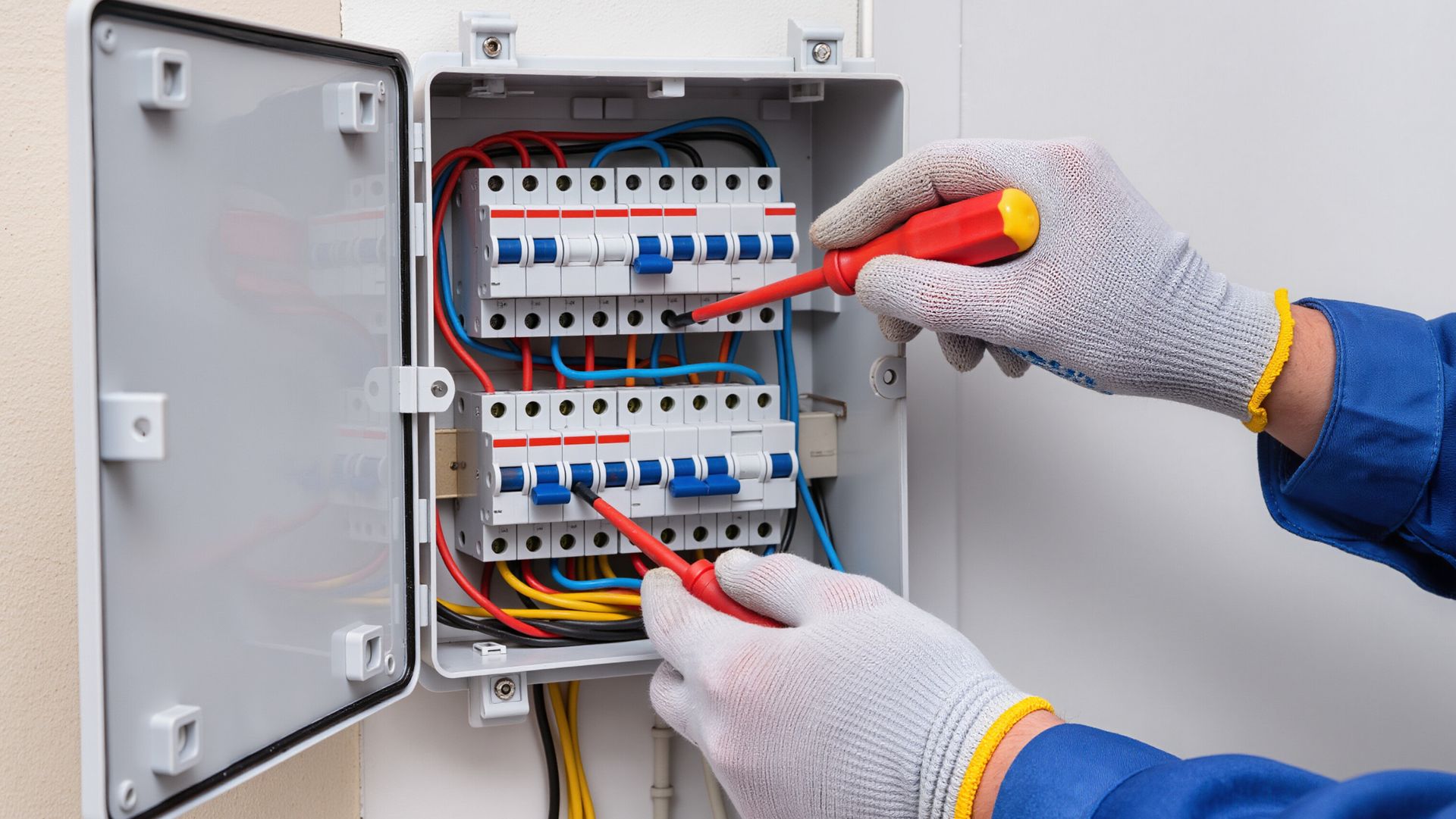 Gloved hands using screwdrivers to adjust circuit breakers inside an open electrical panel box