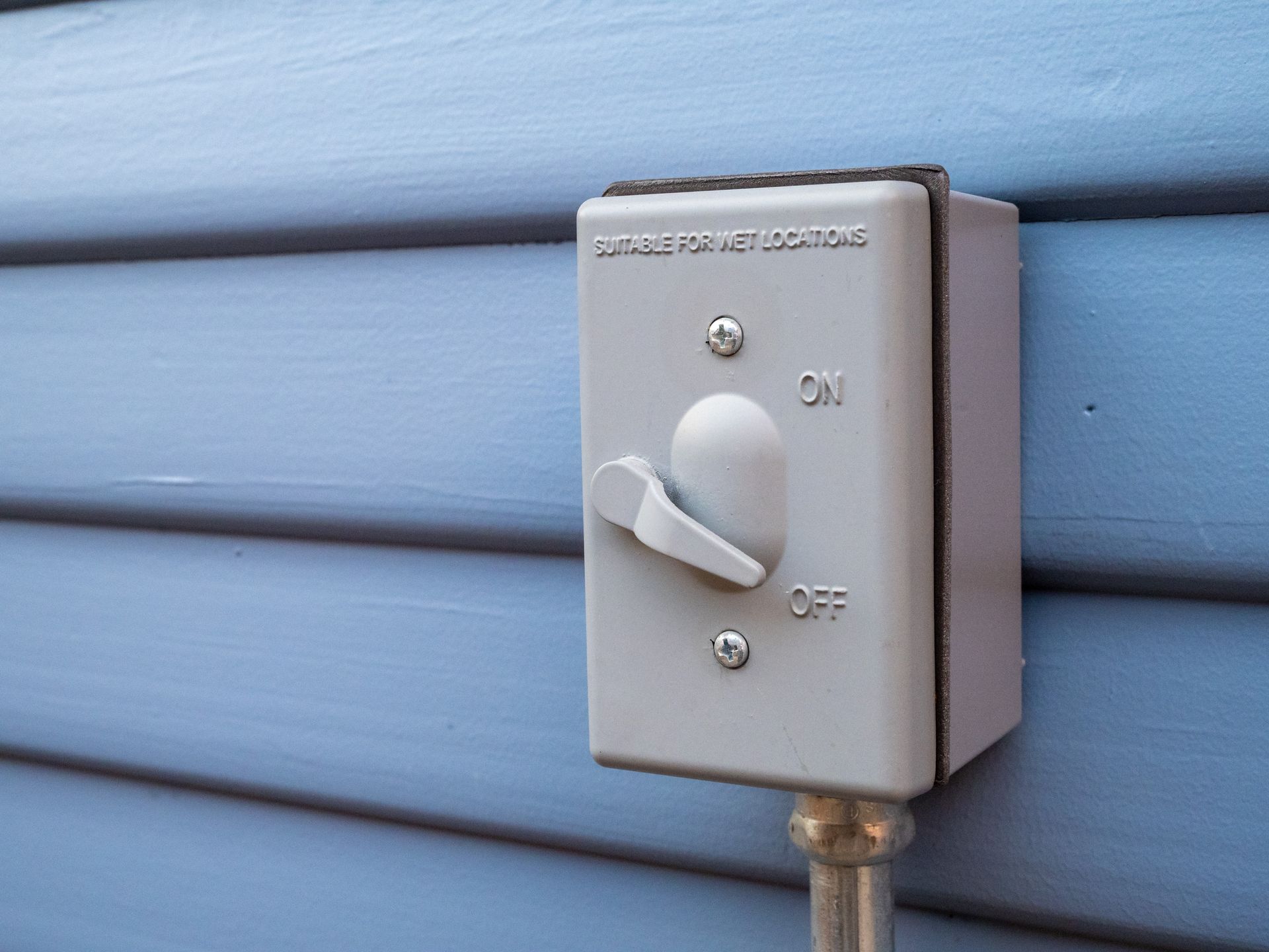 Gray outdoor light switch on blue siding, labeled 