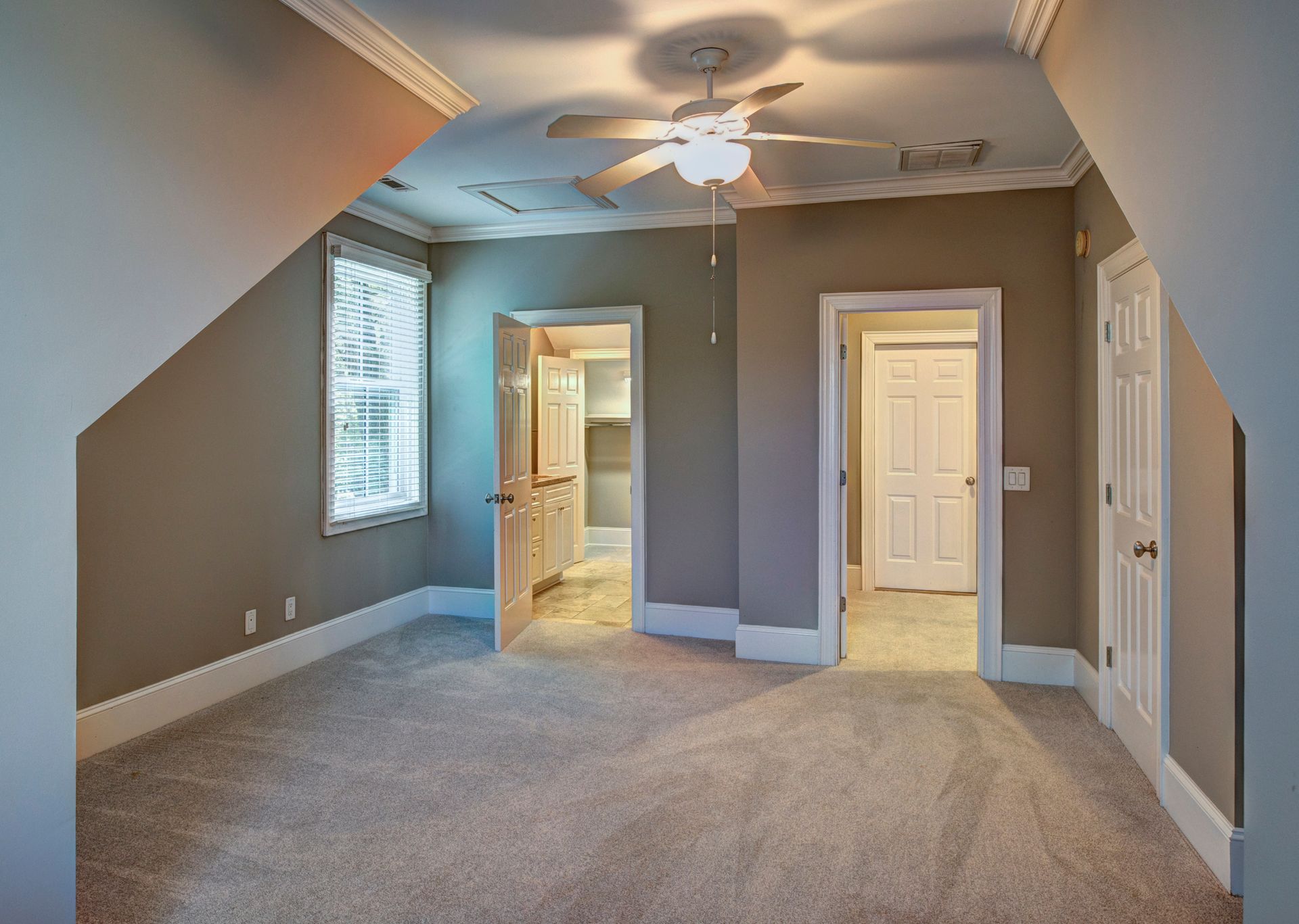 Empty bedroom with beige carpet, gray walls, and three doorways.