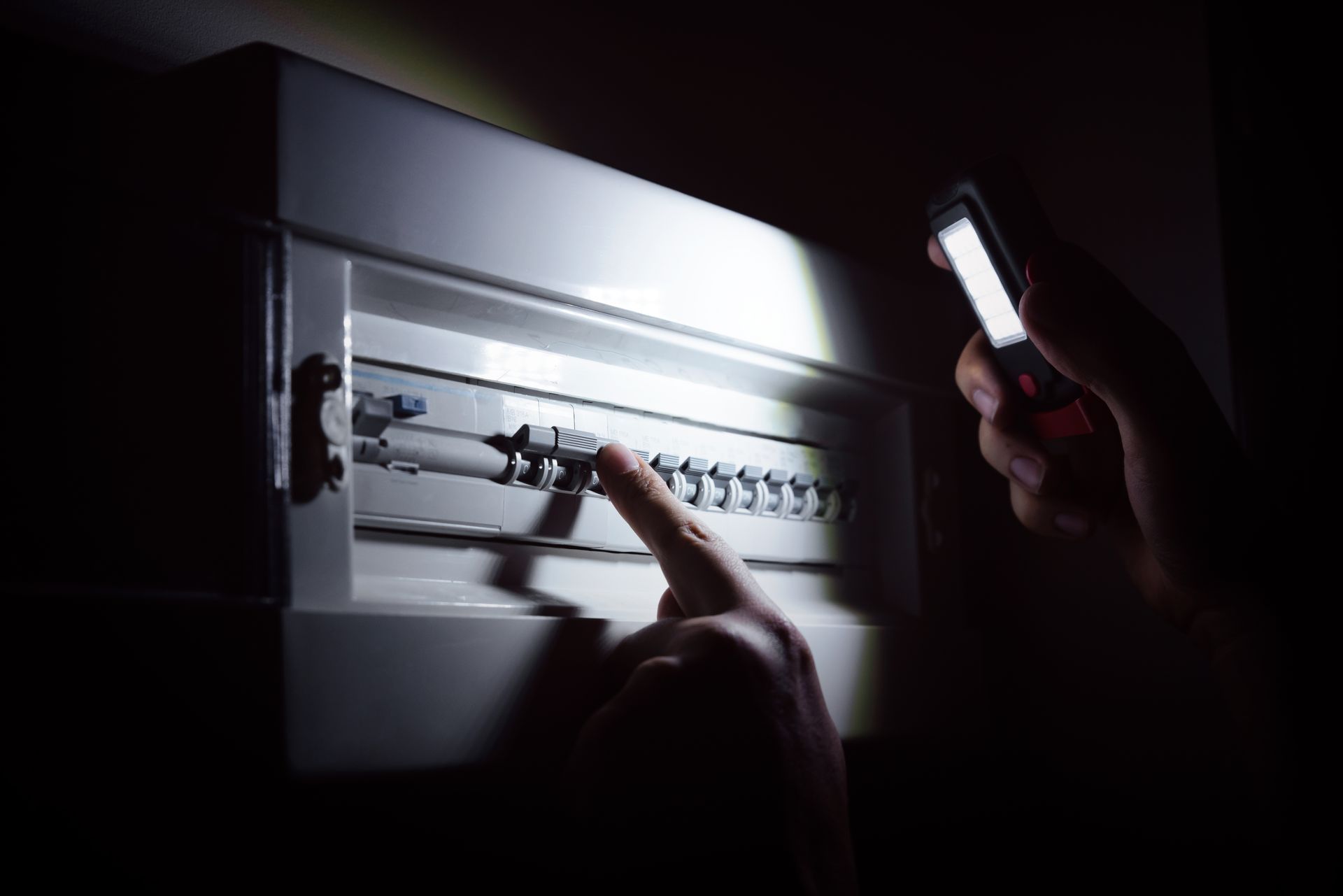 Person using phone flashlight to check electrical circuit breaker box.