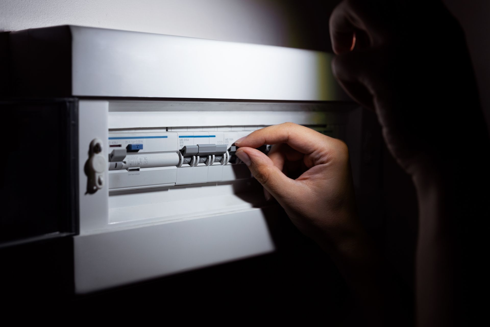 Hand flipping a breaker switch in a dimly lit electrical panel.