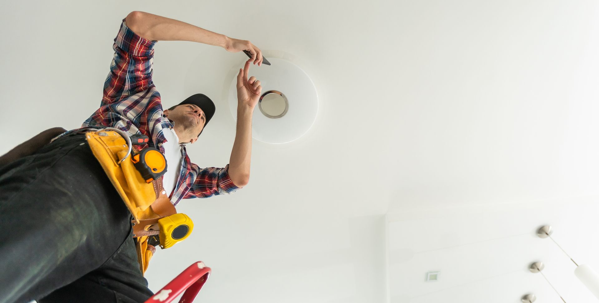 Person on a ladder installing a ceiling light fixture in a white room.