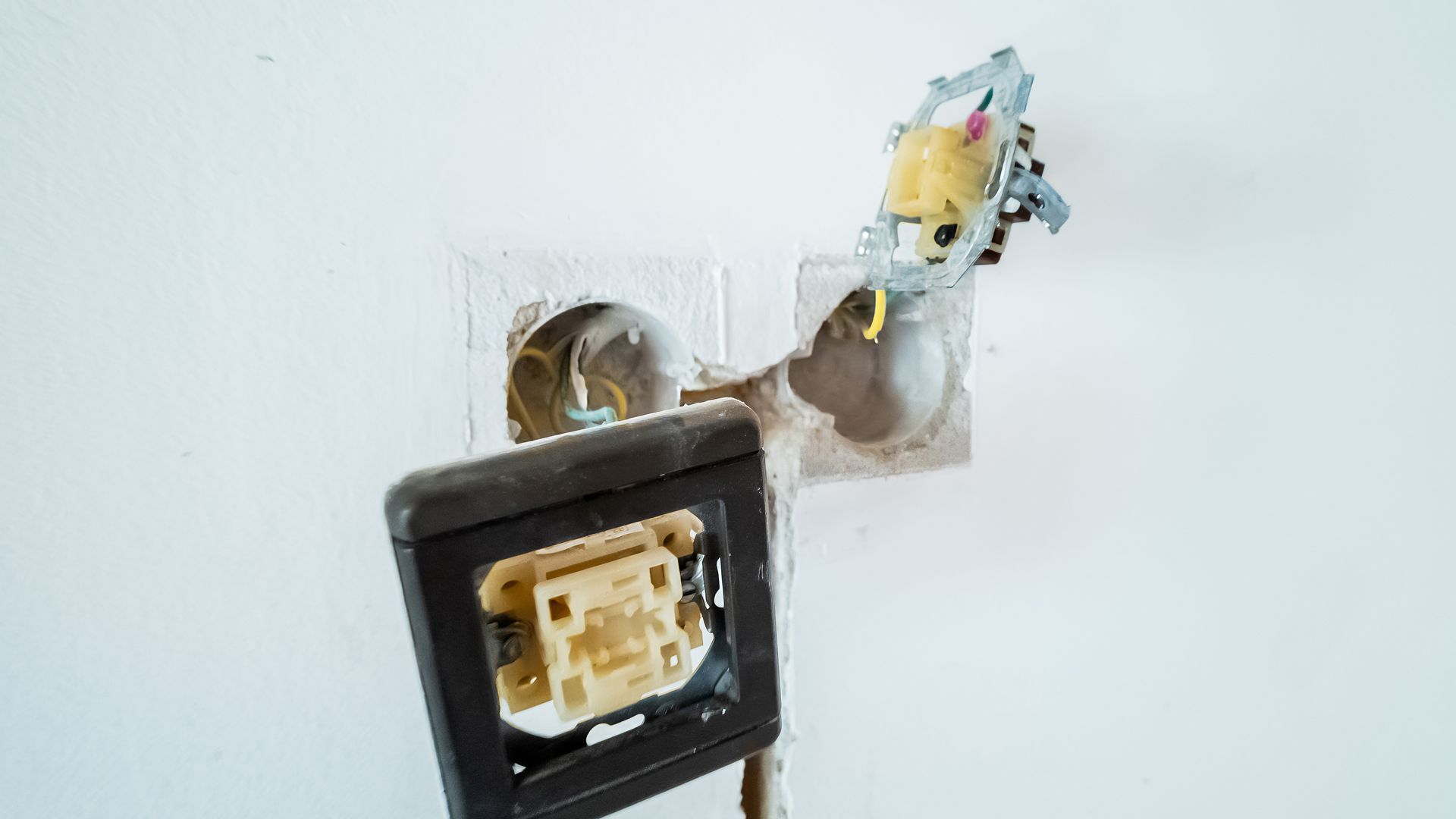Damaged electrical outlets on a white wall; wires exposed; brown and black outlet covers.