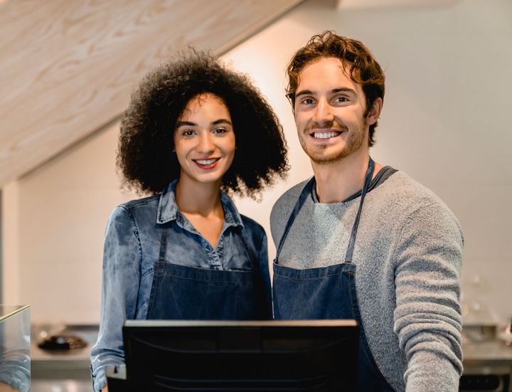 a man and a woman wearing aprons stand in front of a computer monitor