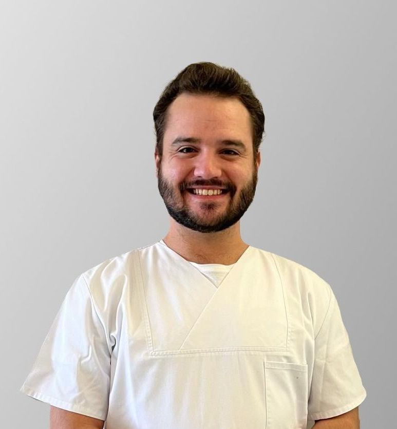 Un homme avec une barbe porte un uniforme blanc et sourit.