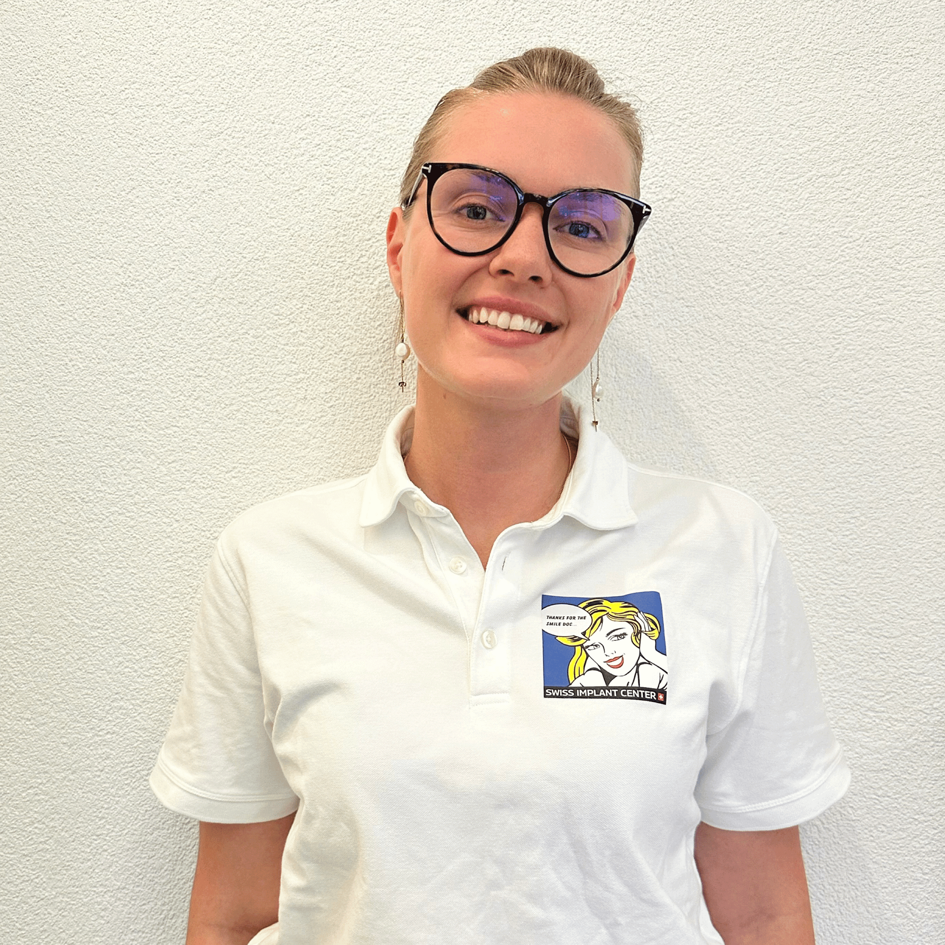 Une femme portant des lunettes et un polo blanc sourit.