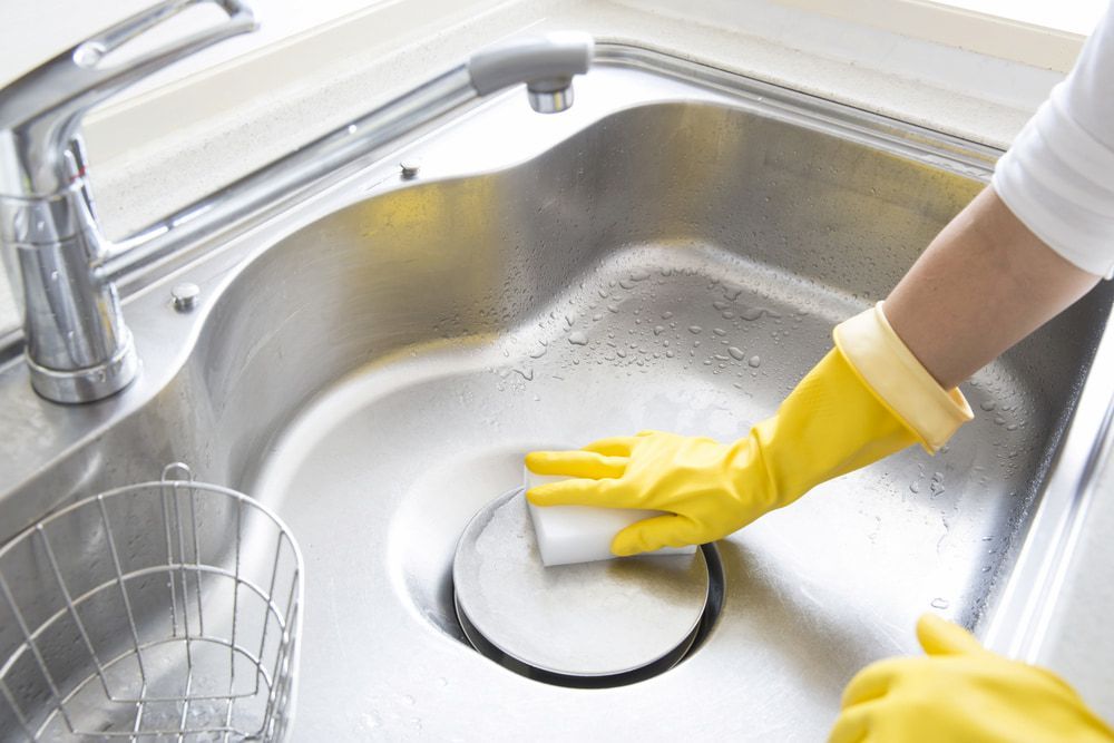 A Person Wearing Yellow Gloves Is Cleaning A Stainless Steel Sink With A Sponge — Proud Cleaning Canberra in Belconnen, ACT