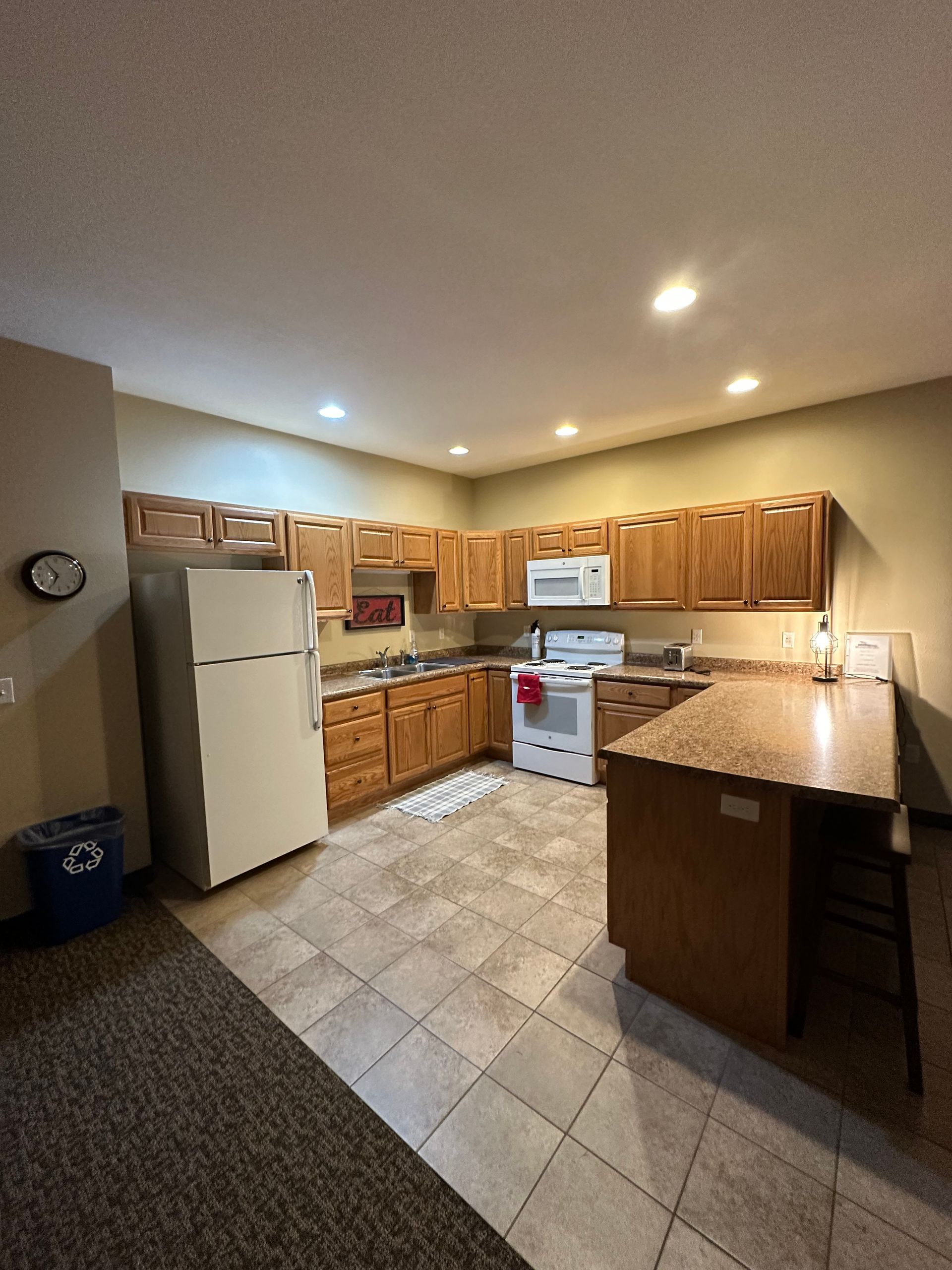 Kitchen with wood cabinets, white appliances, and a tile floor. A breakfast bar is on the right.