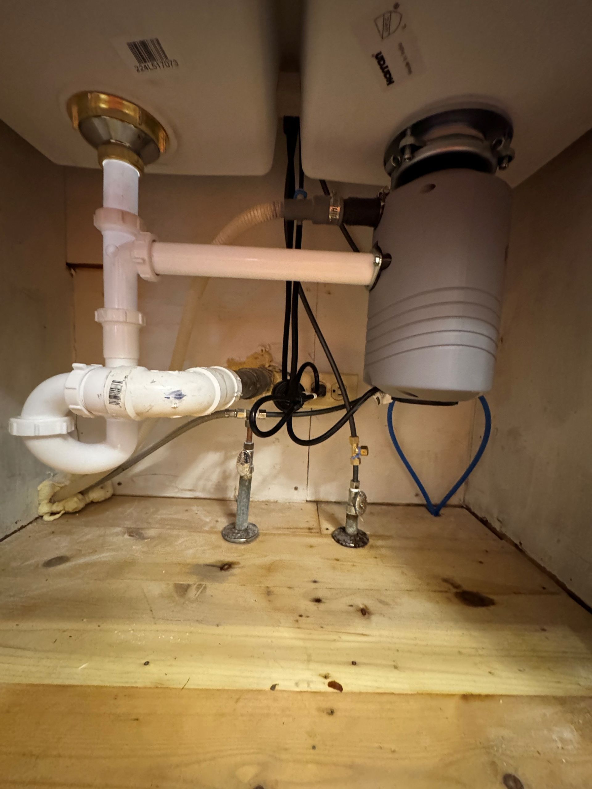 Under-sink plumbing with white pipes, gray disposal, and open cabinet floor