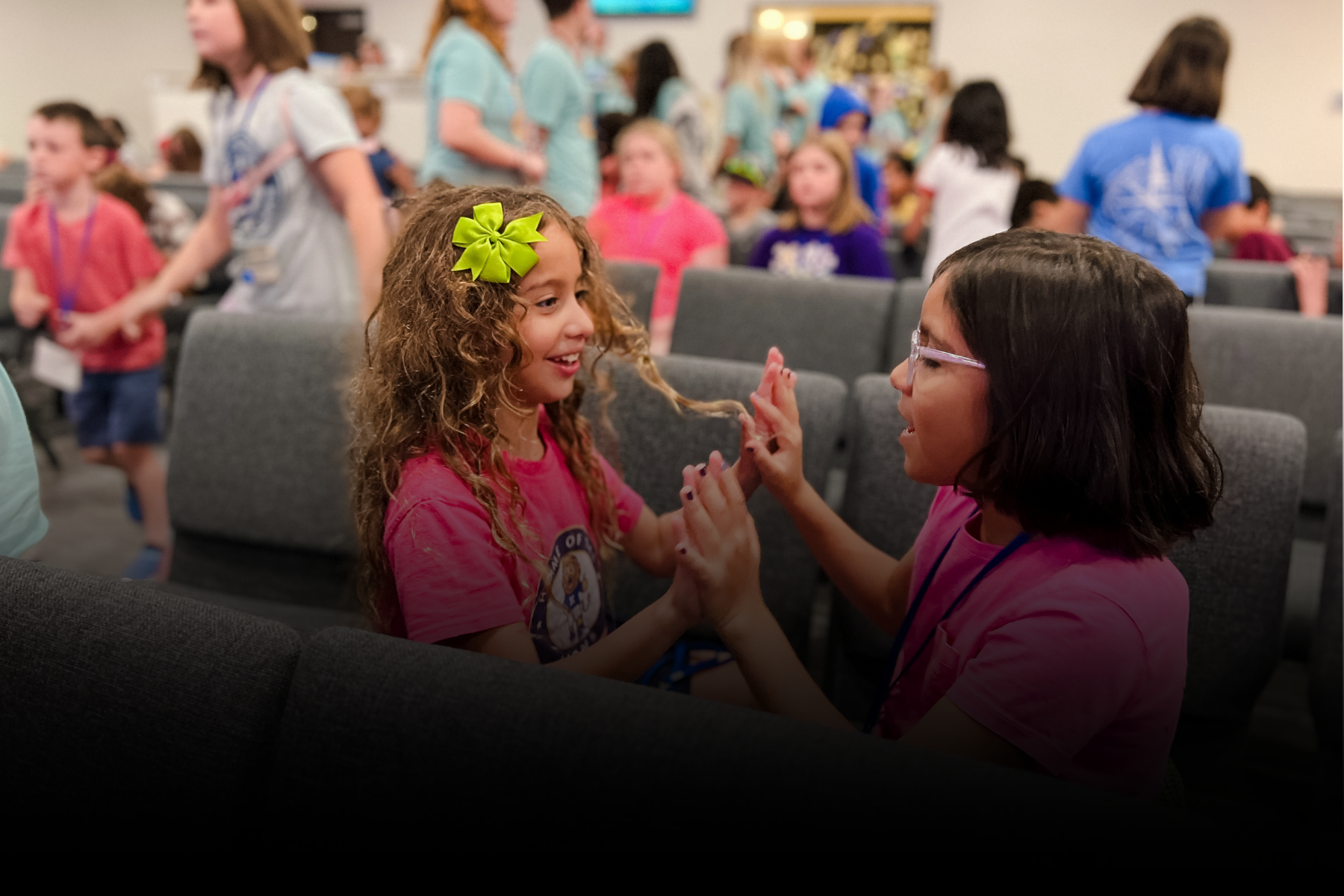Two children smiling and holding hands in a crowded indoor event space