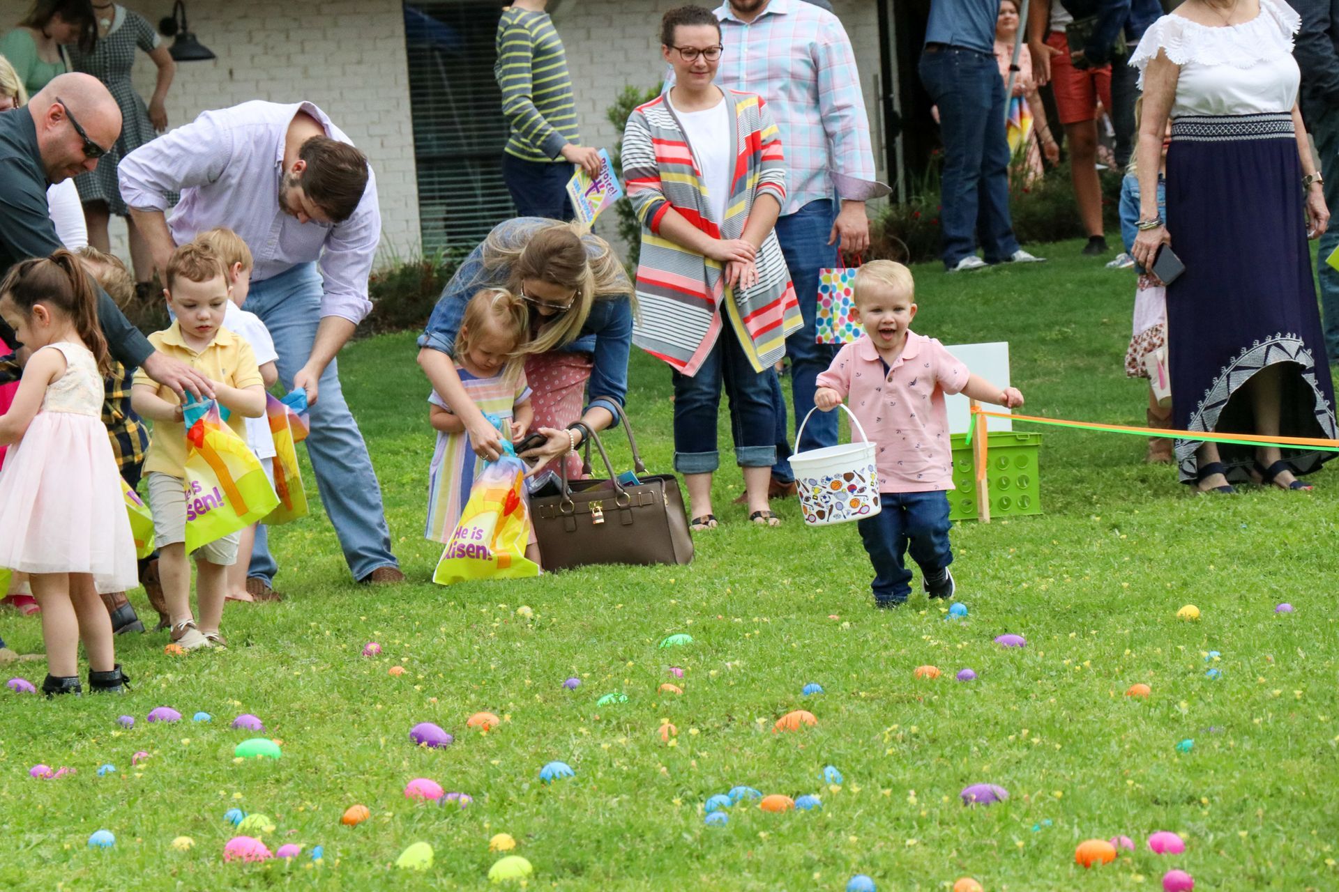 Children and adults in a grassy field collecting colorful eggs during an outdoor event