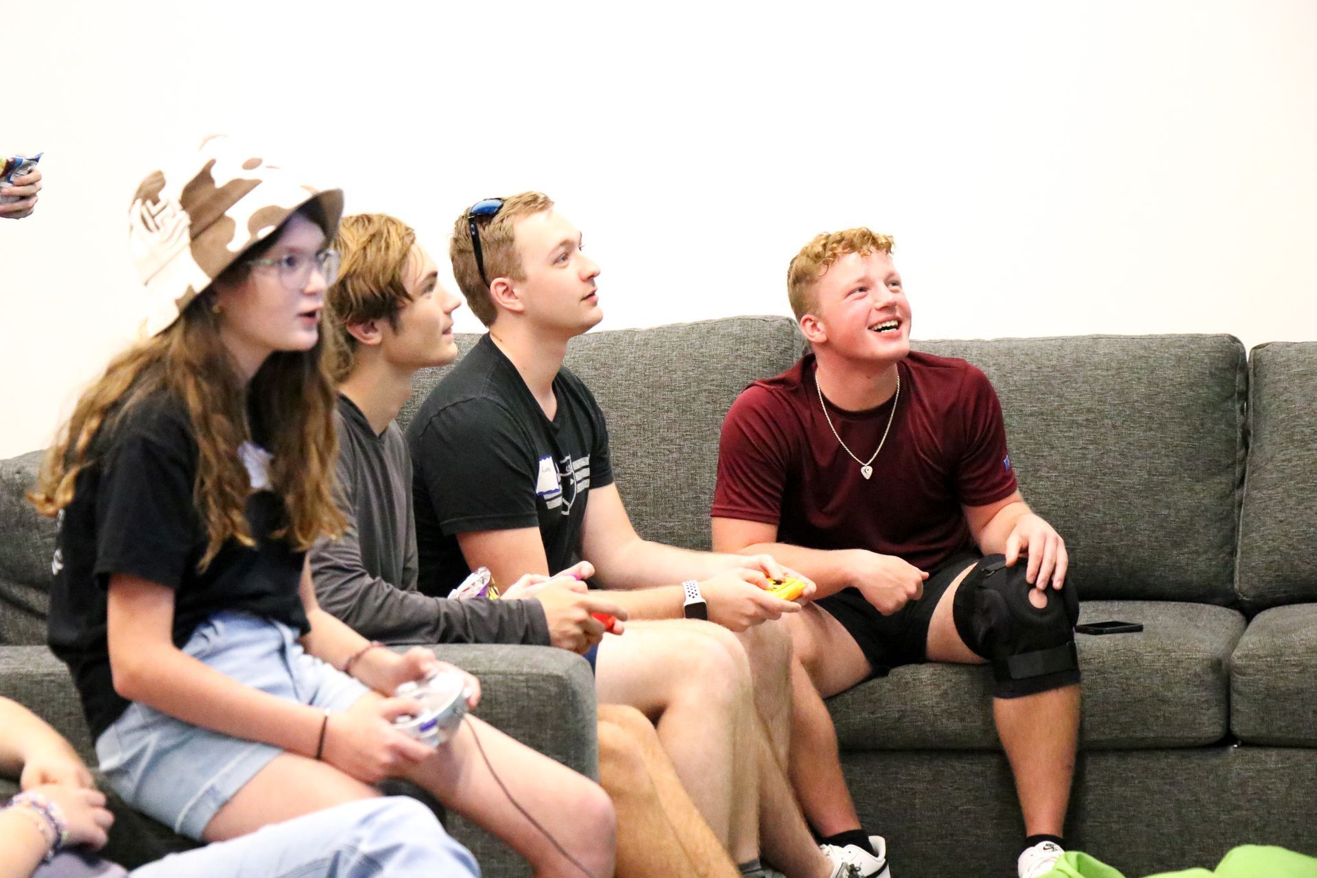 Four people sit on a couch, leaning forward and watching something off-screen.