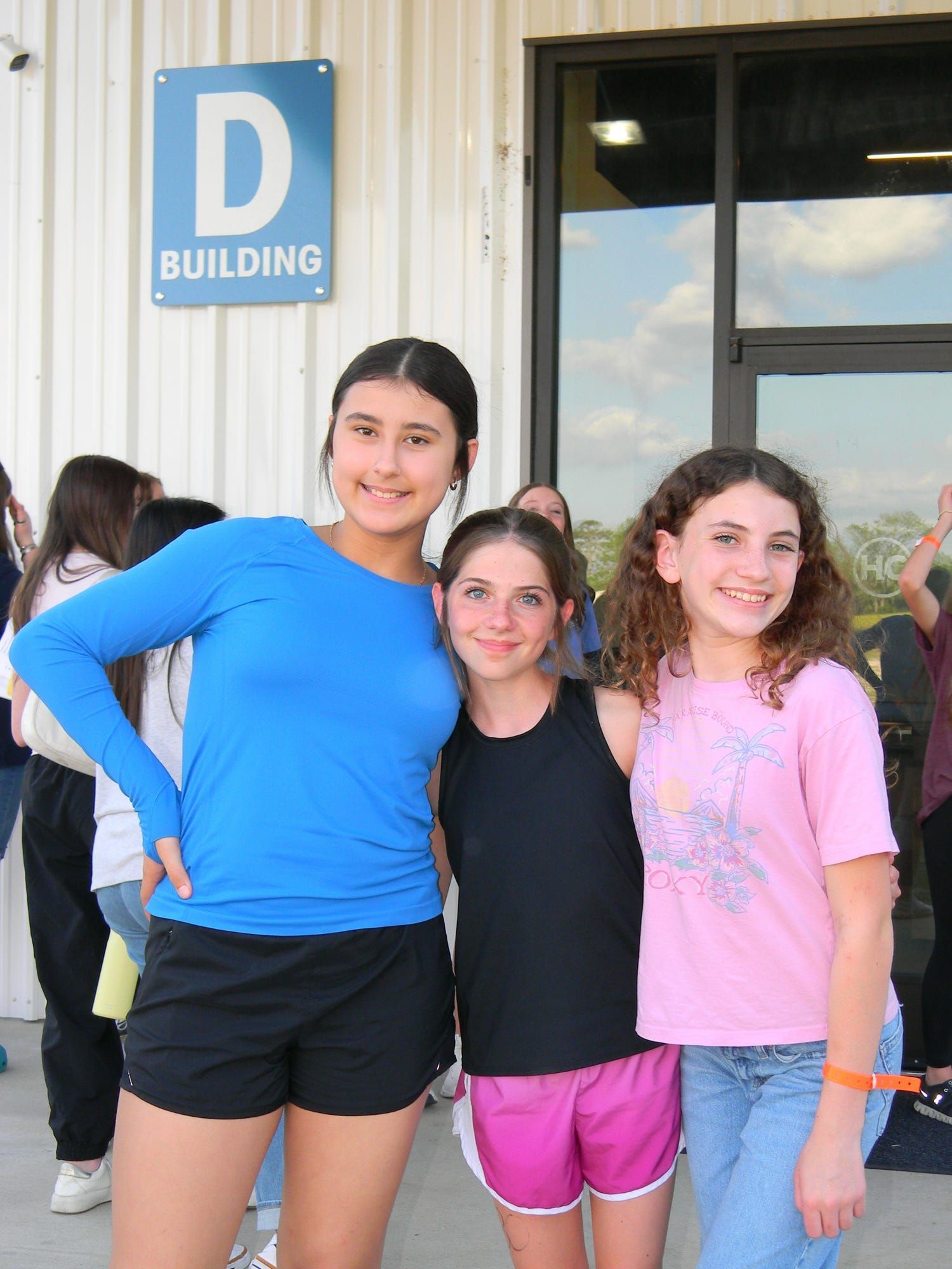 Three young people posing outside a building, smiling at the camera.