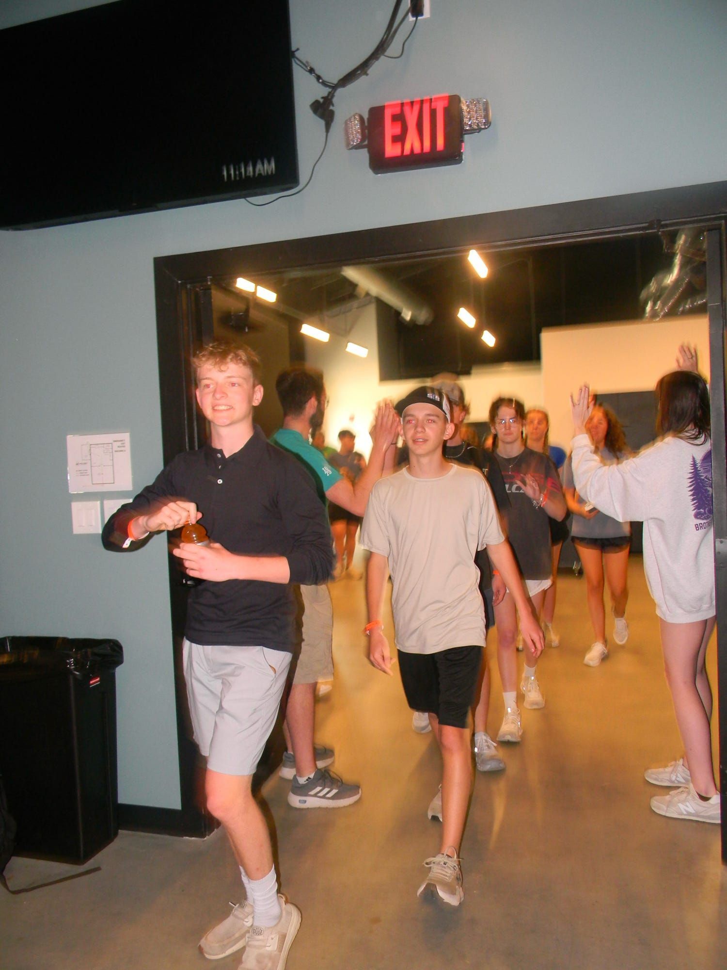 People walking through a doorway under a red EXIT sign in a dim indoor hallway