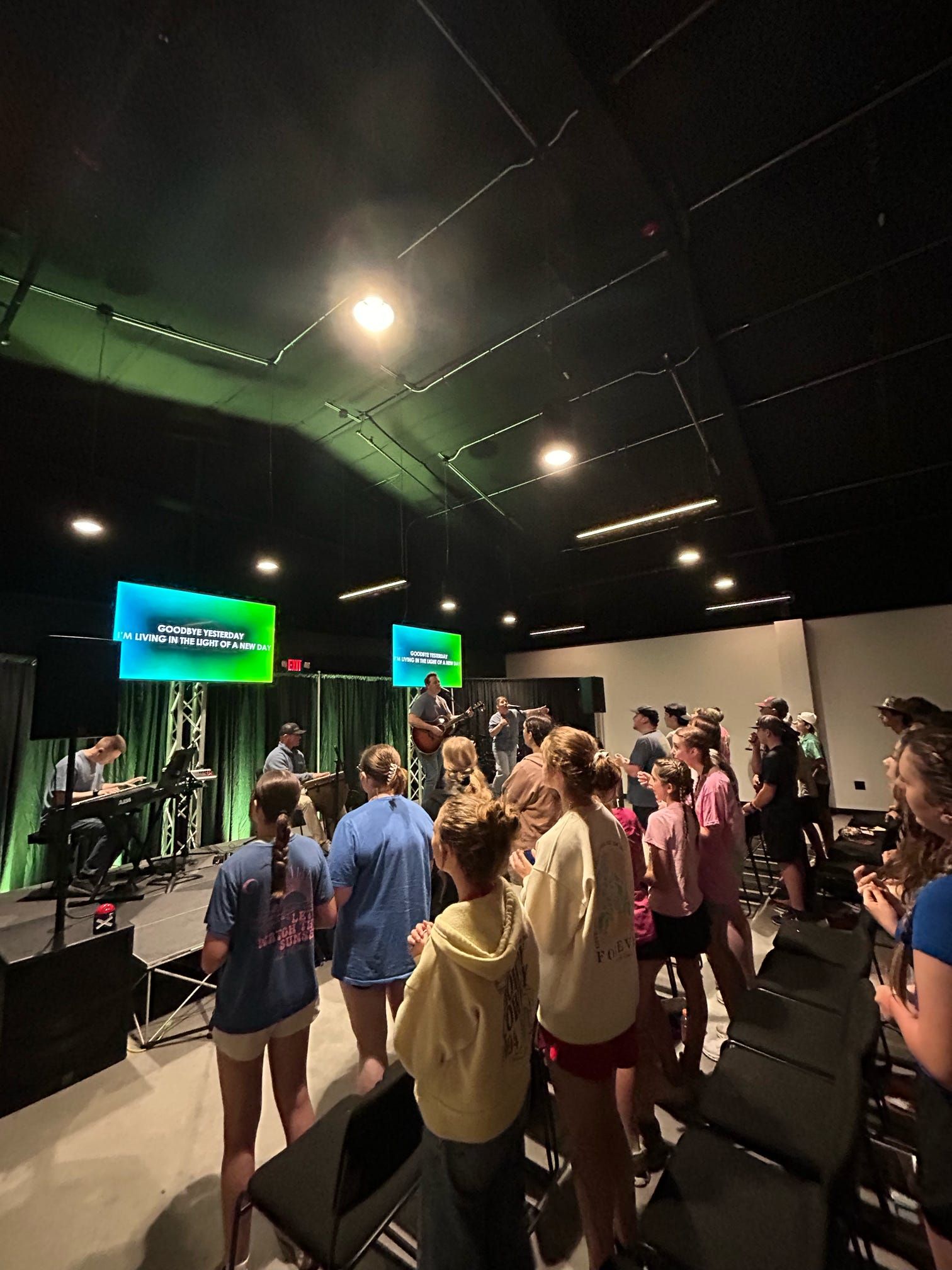 People standing in a black-box studio facing green screens and monitors during a presentation