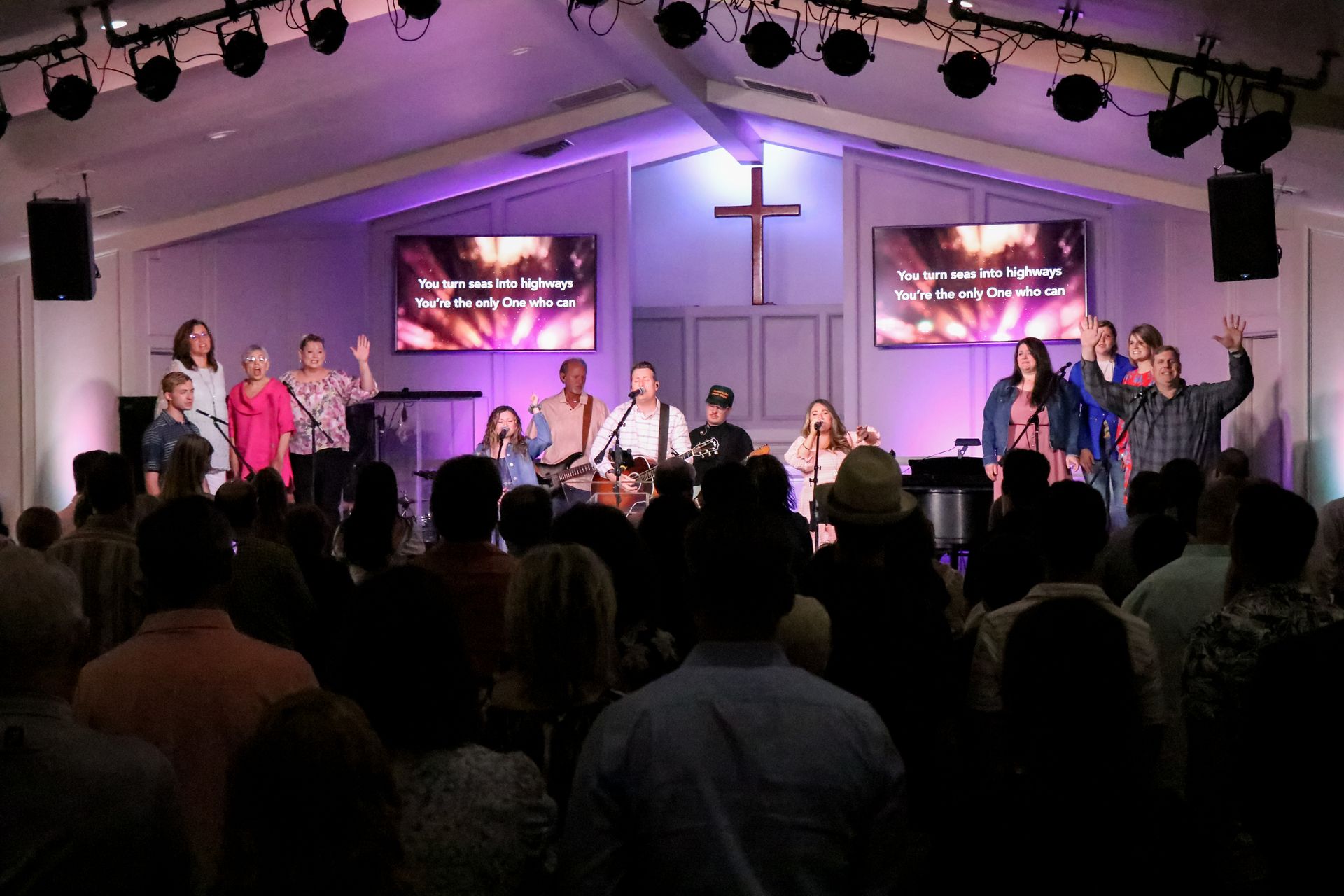 Church worship band onstage under a cross, with audience standing in the foreground