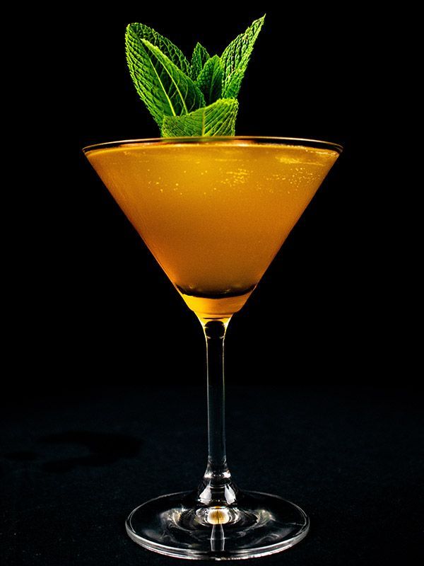 A vibrant yellow cocktail in a martini glass garnished with a sprig of fresh mint, set against a solid black background.