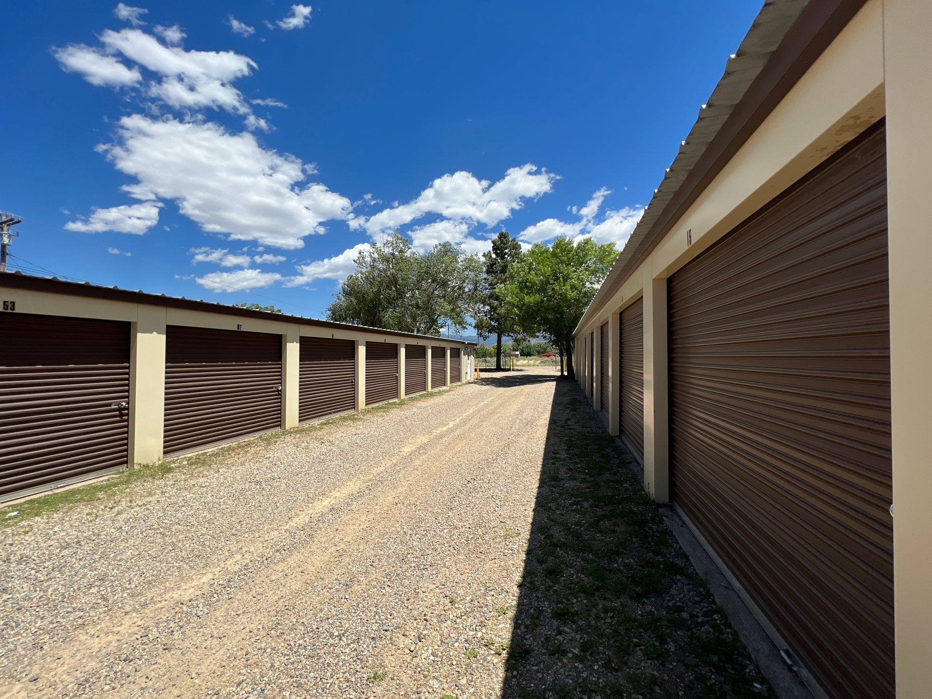 A long row of storage units with dark brown metal doors outside on sunny day with blue sky .