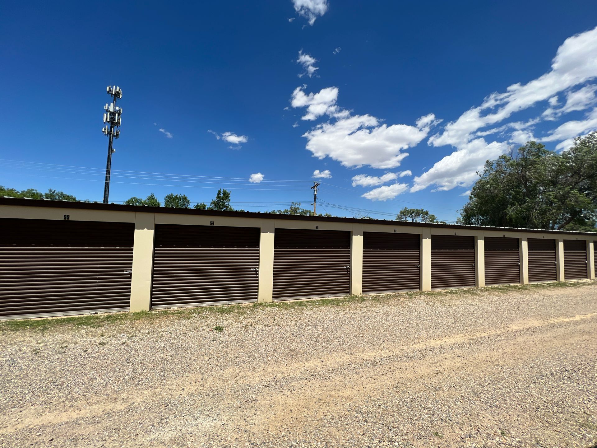 A long row of storage units with dark brown metal doors outside on sunny day 