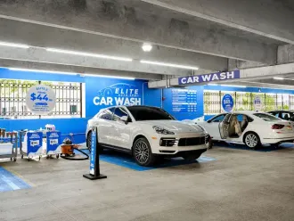 A car wash with two white cars inside. Blue and white color scheme. Sign says