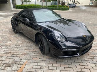 Black Porsche convertible parked on brick pavers.