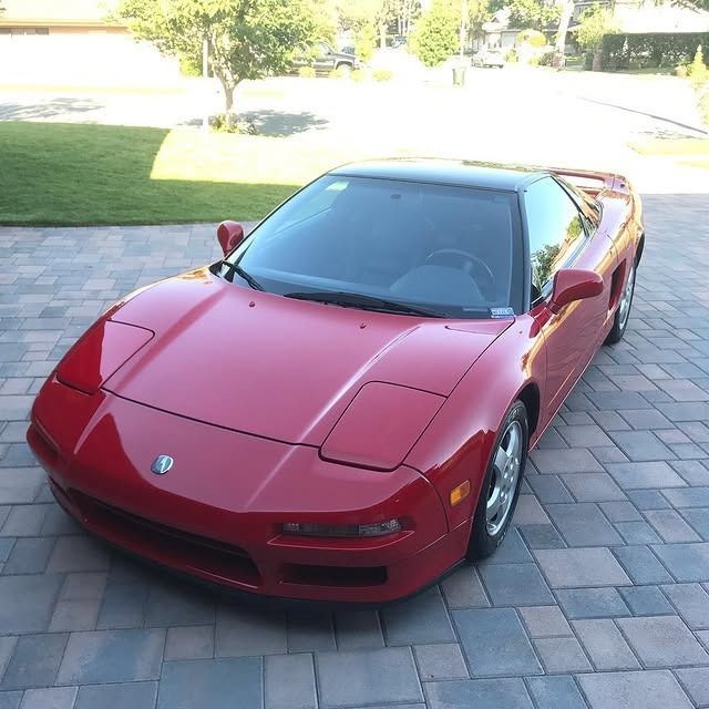 Red Honda NSX sports car parked on a brick driveway. Black roof, shiny finish.