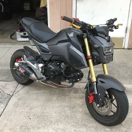 Modified gray Honda Grom motorcycle with gold forks, black seat, and red accents parked on concrete.