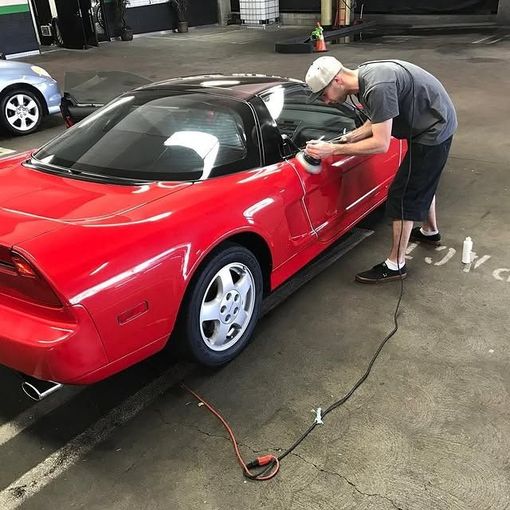 Man polishing a red sports car. He's using a power buffer in an indoor garage setting.