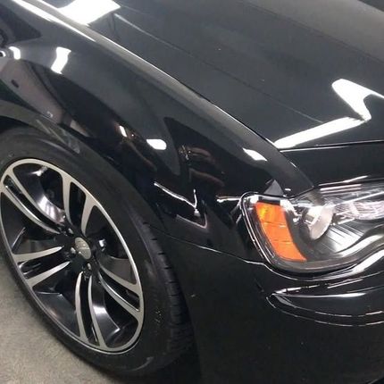 Black Chrysler 300 car with a glossy finish, showing the front tire and headlight, in a well-lit garage.
