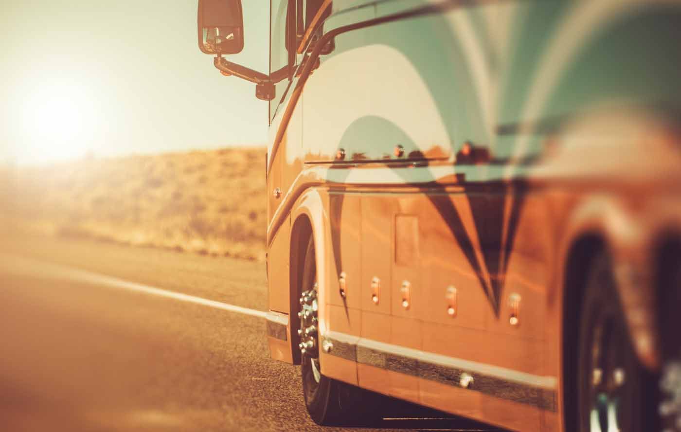 Orange tour bus on a highway, reflecting the landscape, with a bright, sunny sky.